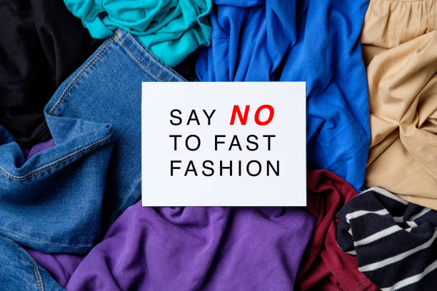 Say NO to fast fashion sign on white paper over heap of female clothes